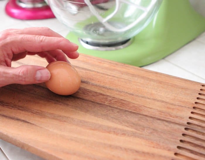 A hand placing a hard boiled egg on a cutting board