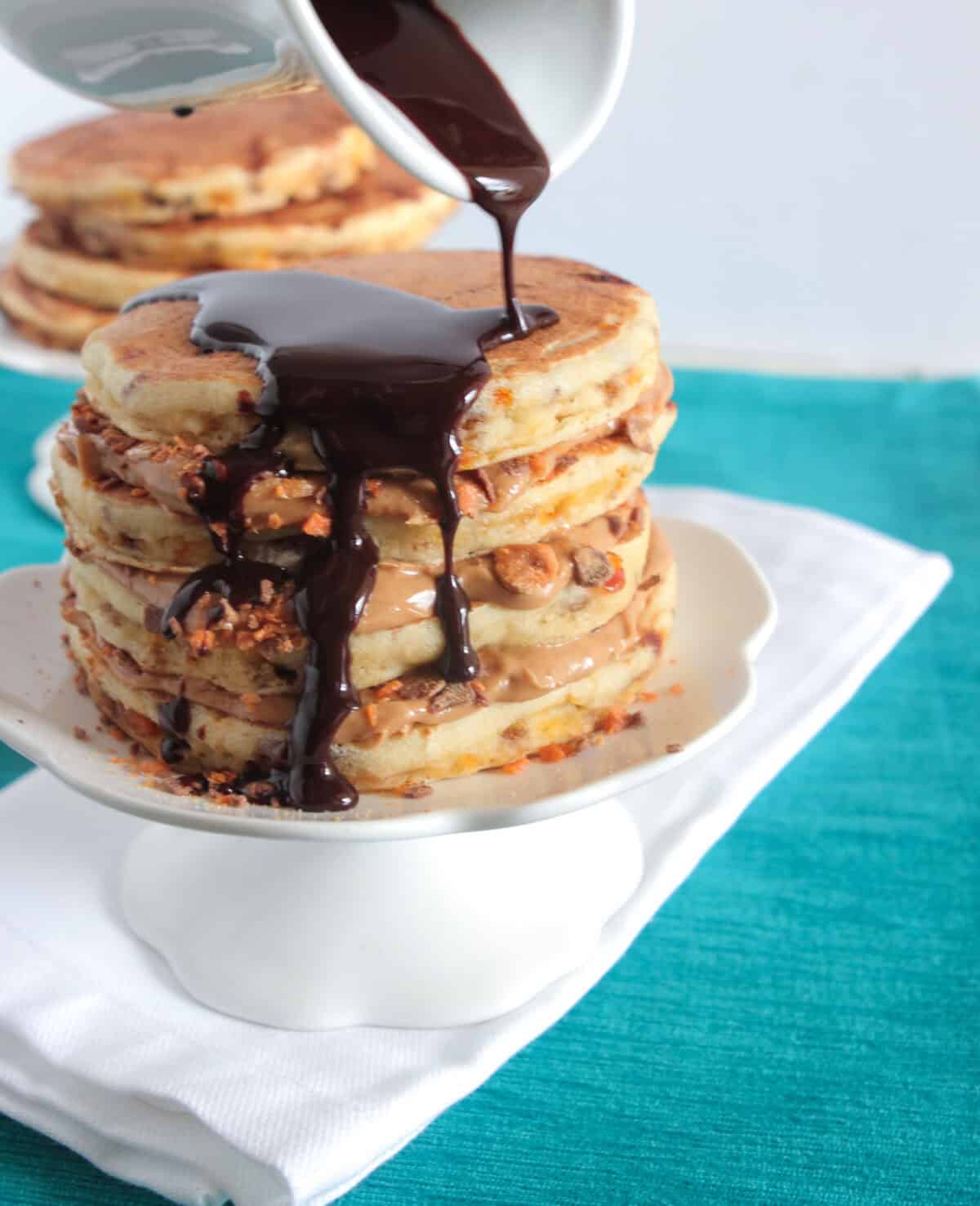 pouring chocolate sauce over stack of peanut butter pancakes