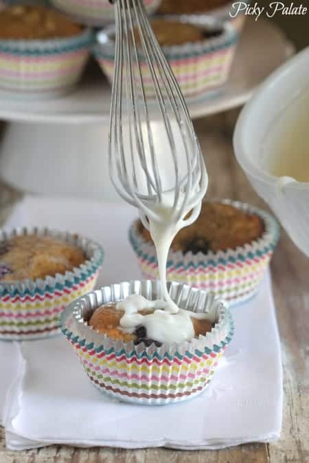 A blueberry banana bread muffin is topped with icing dripping from a whisk.