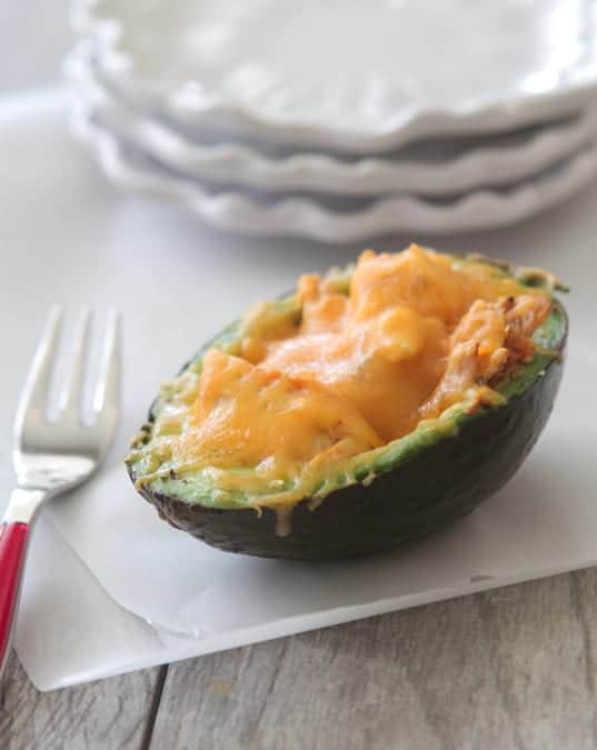 A cheesy baked avocado stuffed with chicken on a clear cutting board.