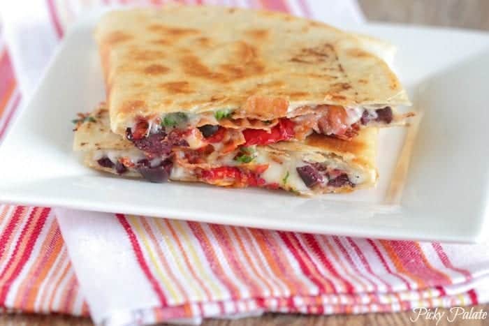 Two halves of a Mediterranean bacon quesadilla stacked on a white square plate.
