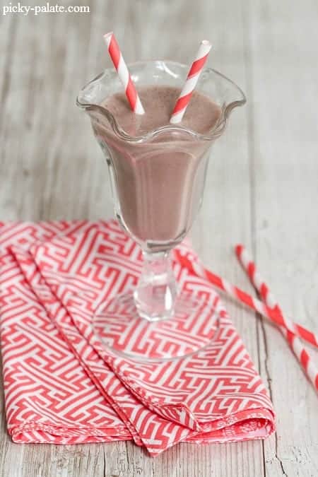 A chocolate banana peanut butter smoothie in a fountain glass with two red-striped straws.
