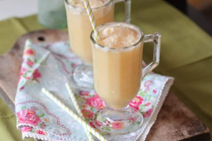 Two side-by-side honey and orange creamsicle slushies on a floral cloth, with straws.