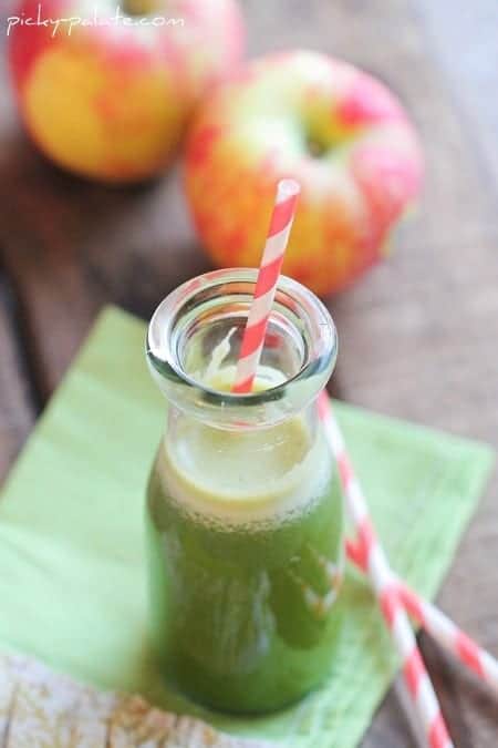 Green juice in a glass with a red-striped straw, with apples in the background.