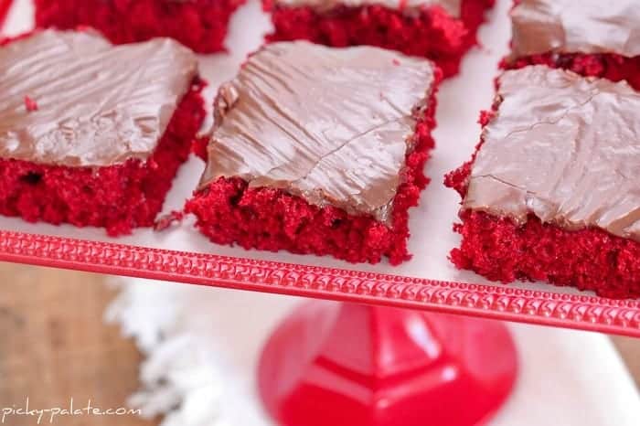 Red velvet sheet cake squares on a red cake stand.