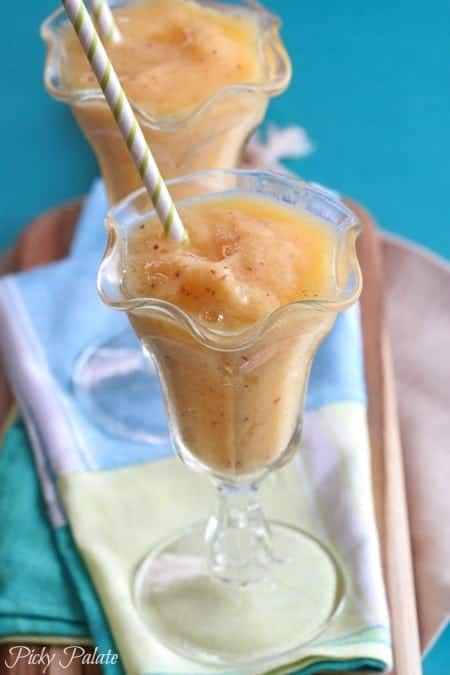 A mango peach slushy in a fountain glass with a straw.