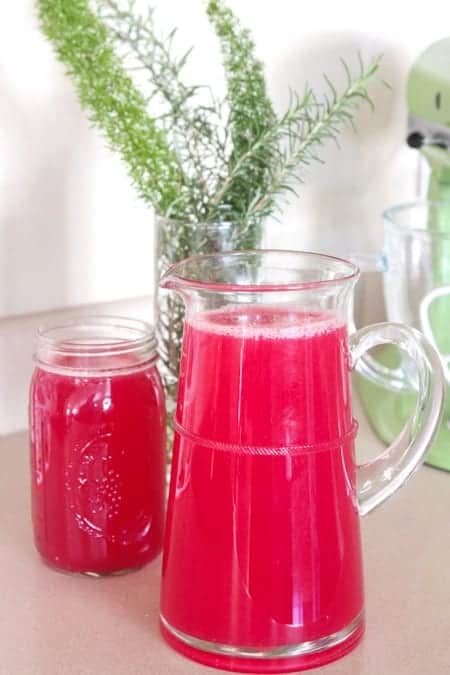 A clear pitcher of blueberry lemonade next to a full glass.