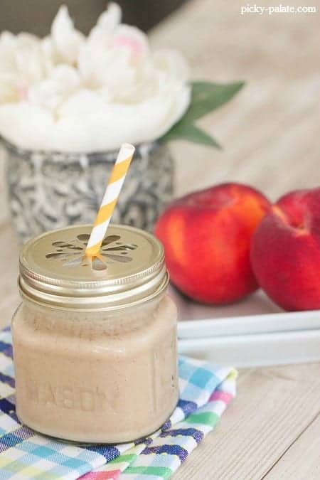 A peaches and cream frosty in a glass mug with a lid and a yellow-striped straw.