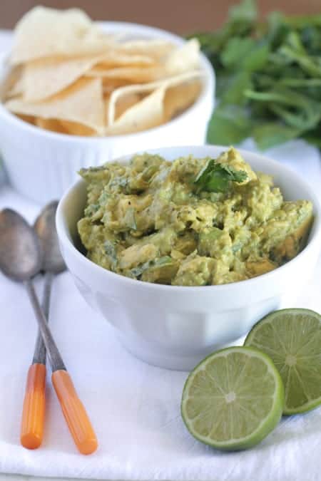 A bowl of restaurant-style guacamole next to limes and a bowl of tortilla chips.