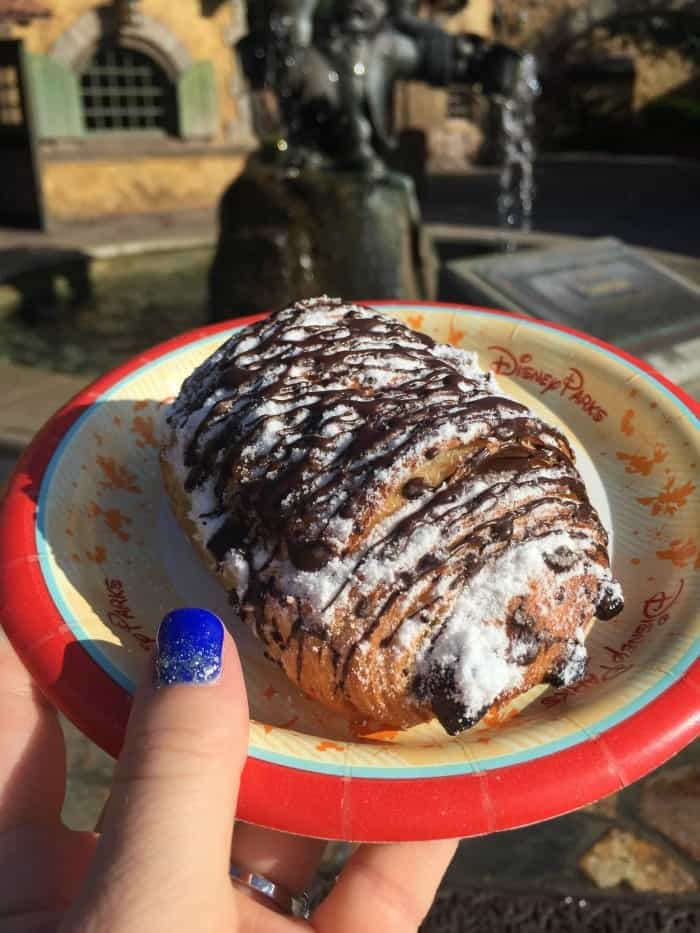 A Large Chocolate Croissant Topped with Powdered Sugar and Chocolate Drizzle