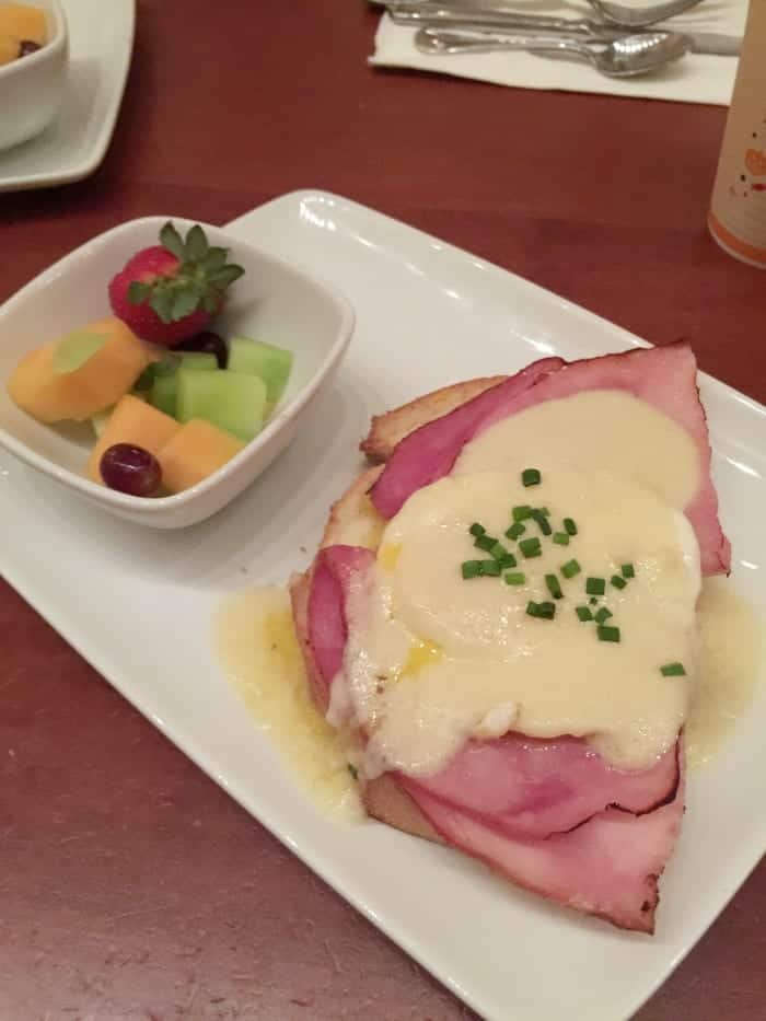 An Open Face Croque Madame on a Plate Beside a Bowl of Fruit