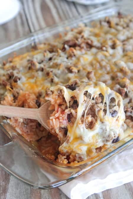 A Wooden Spoon Scooping Out a Serving of Enchilada Rice Bake From the Pan