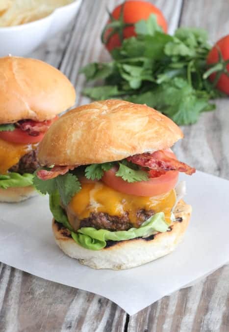 Two Taco Bacon Cheeseburgers on a Napkin Next to Greens and Tomatoes