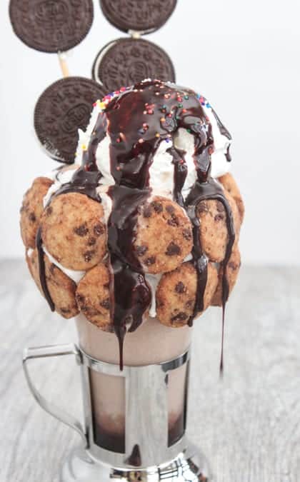 A chocolate cookie and peanut butter milkshake in a fountain glass drizzled with chocolate.