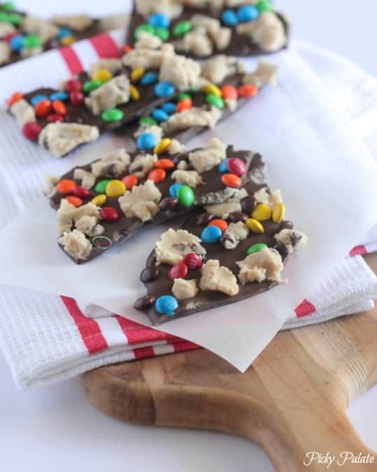 Chocolate cookie dough bark on a sheet of parchment paper over a red-and-white striped cloth, on top of a wooden board.