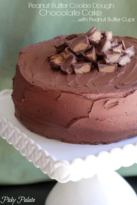 A while peanut butter chocolate cake frosted and garnished with peanut butter cups on a cake stand.