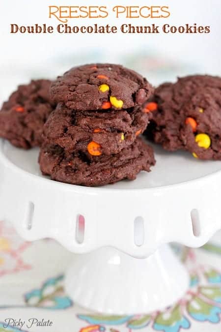 Reese's Pieces double chocolate chunk cookies stacked on a cake stand.