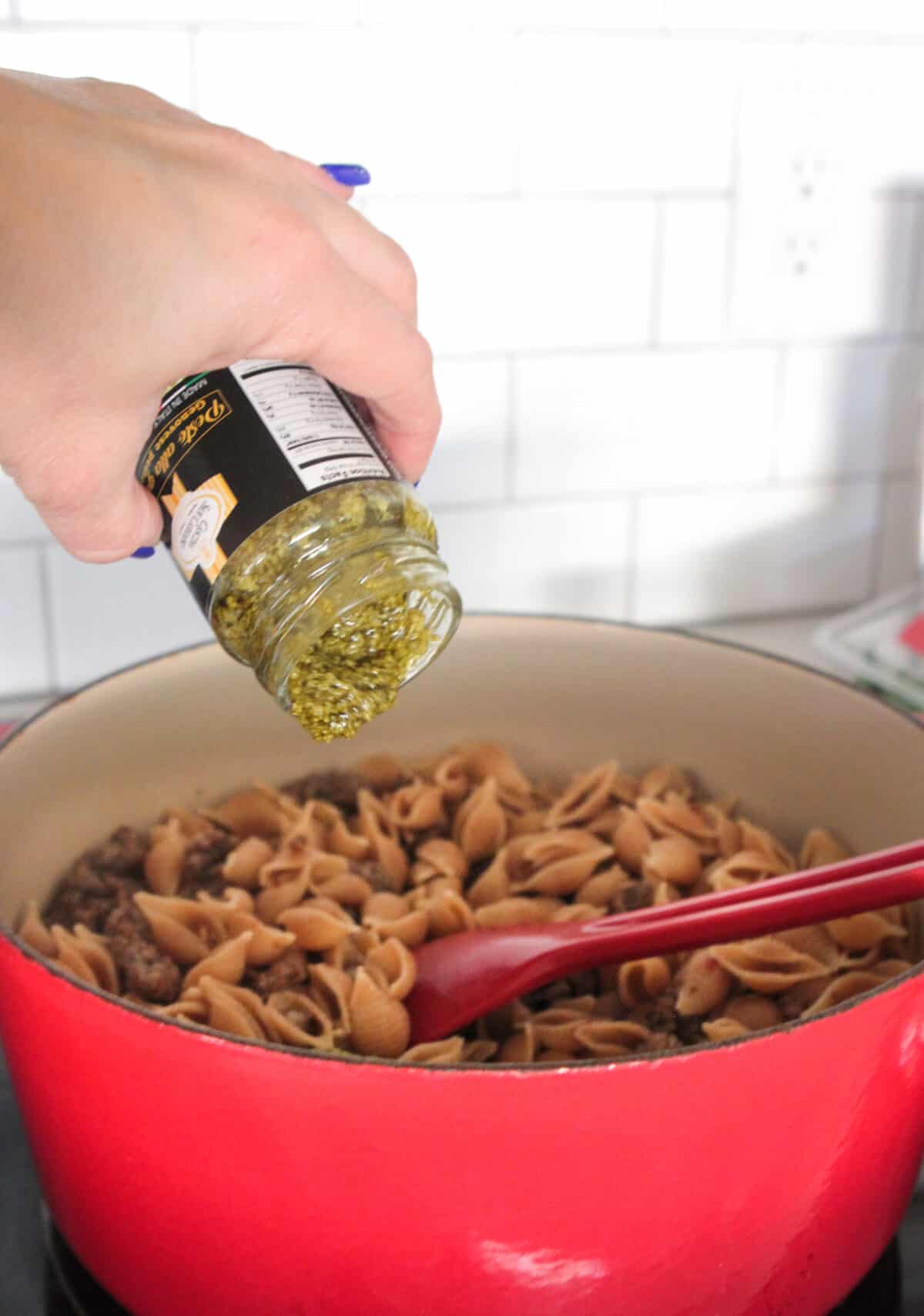 adding pesto to sausage pasta