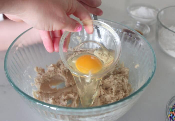 adding egg to cookie dough mixing bowl