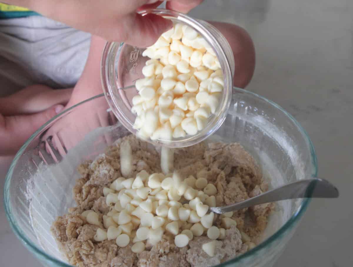 adding white chips to cookie dough mixing bowl
