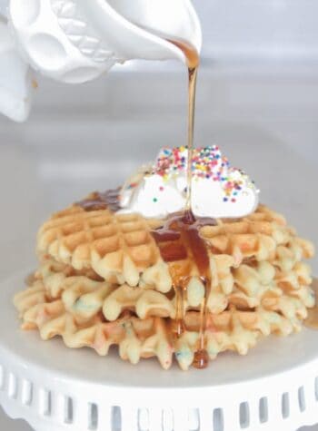 A Stack of Birthday Cake Waffles with Syrup Being Poured Overtop