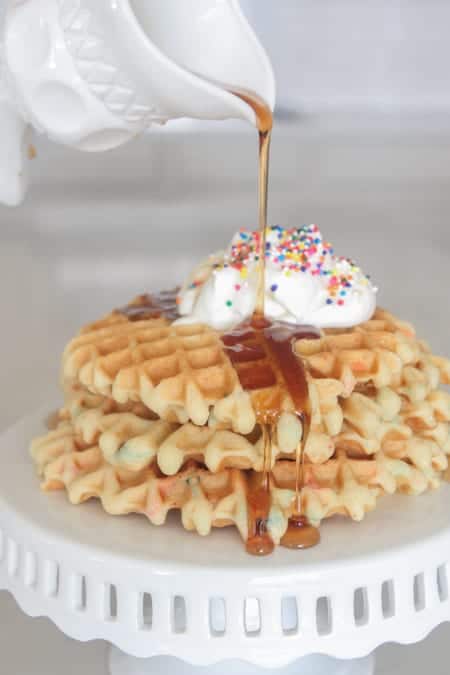 Three Birthday Cake Waffles on a White Cake Stand with Whipped Cream on Top