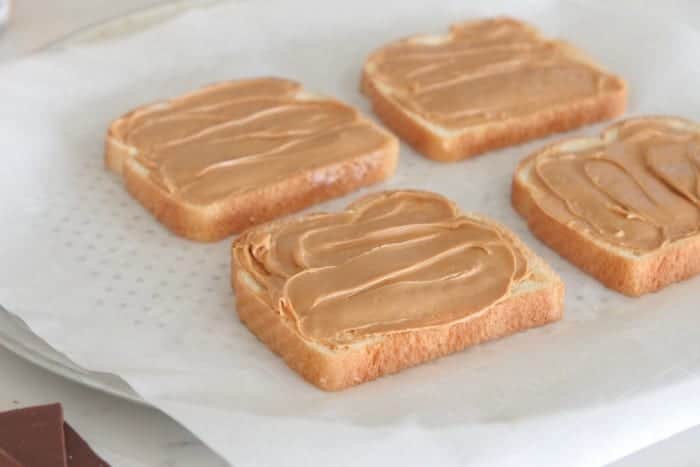 Four bread slices topped with peanut butter.