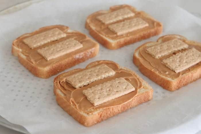 Four bread slices topped with peanut butter and Graham crackers.