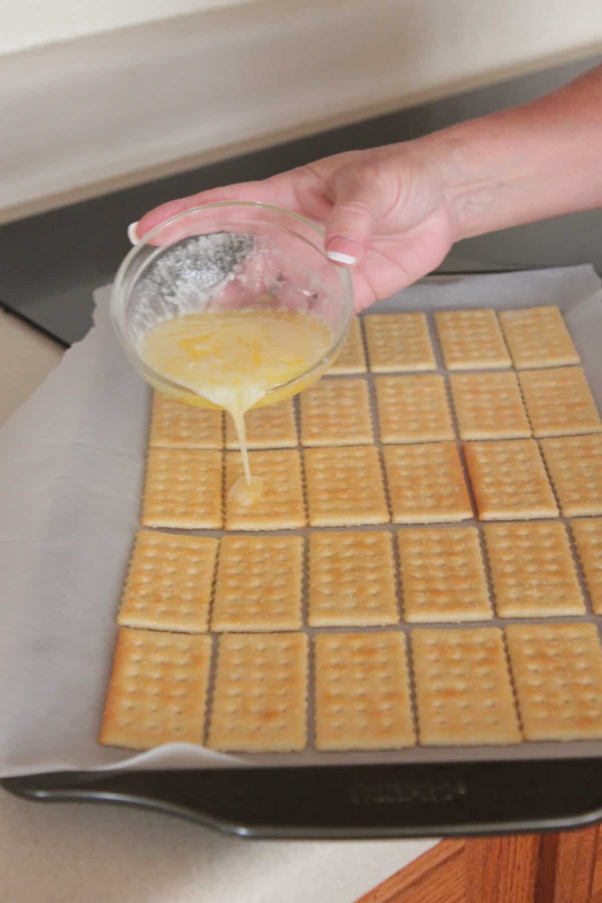 pouring melted butter over club crackers on cookie sheet