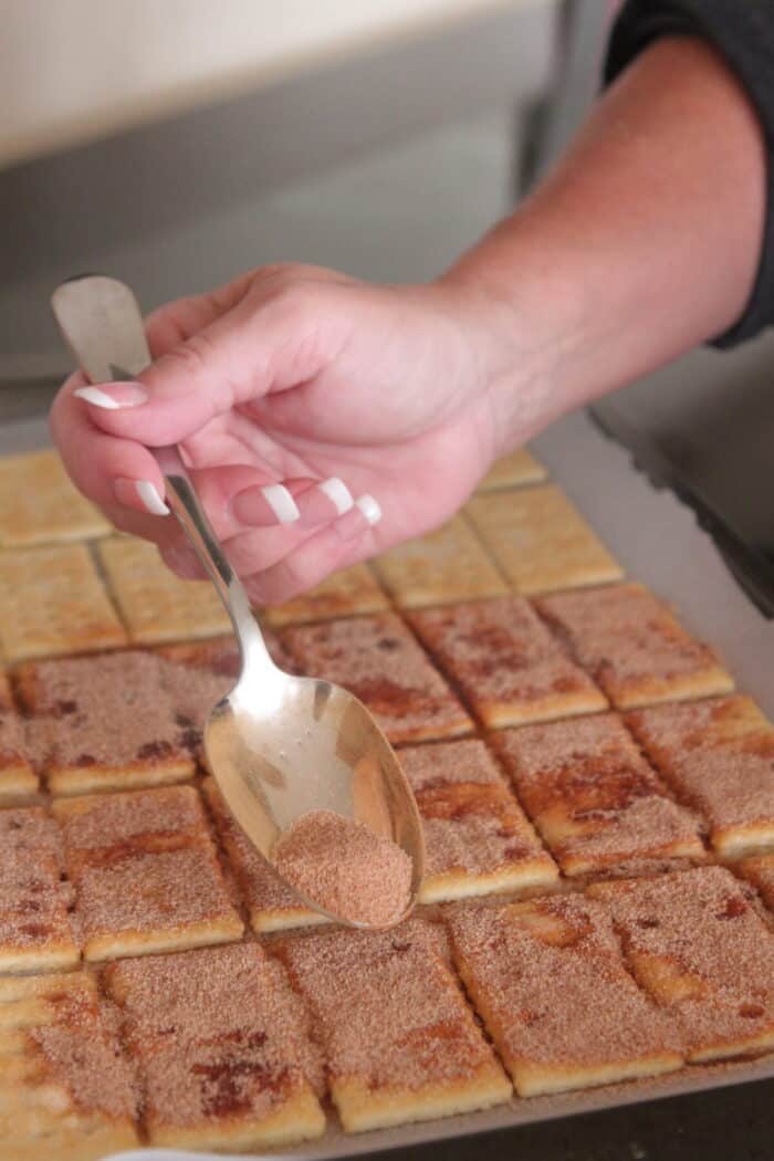 sprinkling cinnamon sugar over buttered club crackers on cookie sheet