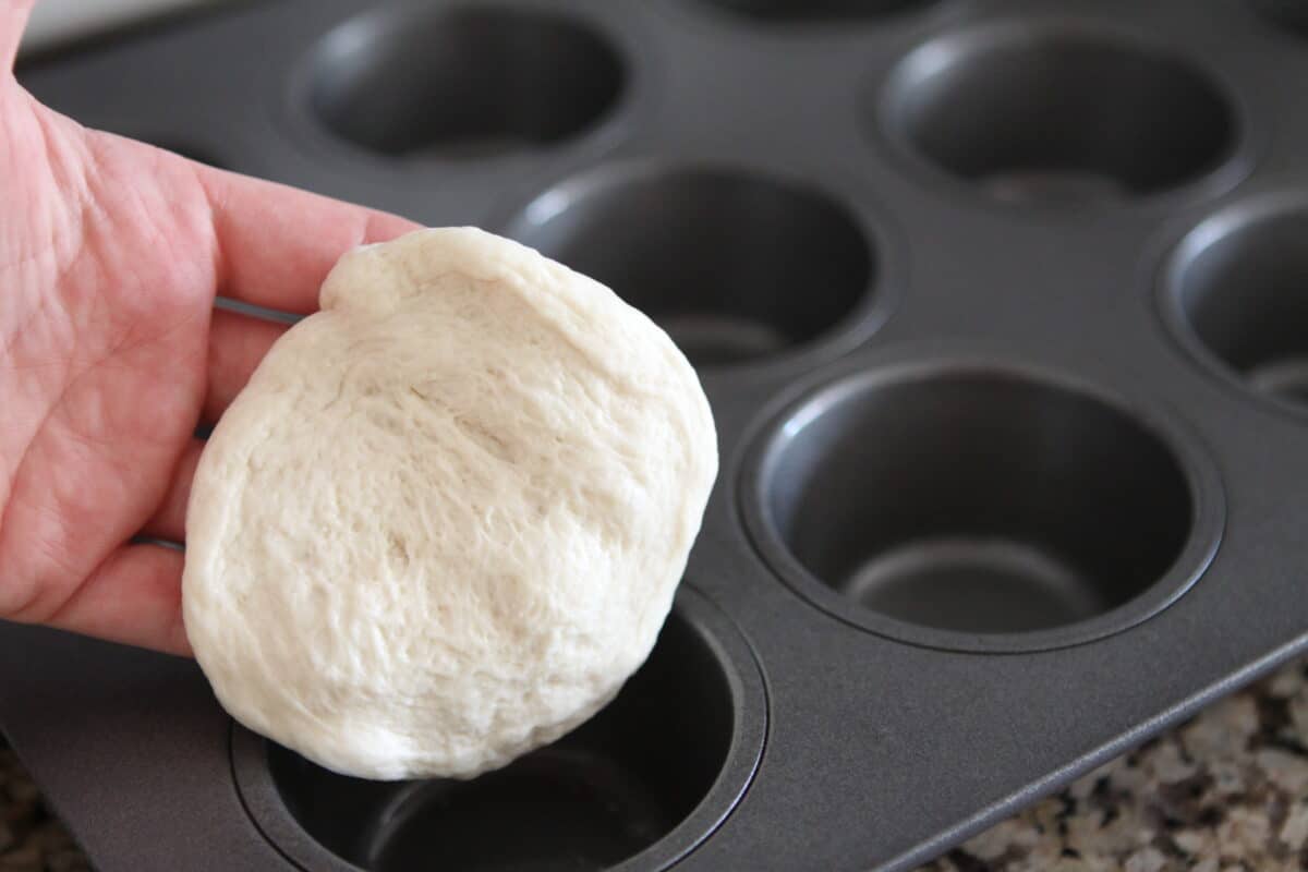 pressing bread dough into muffin tin