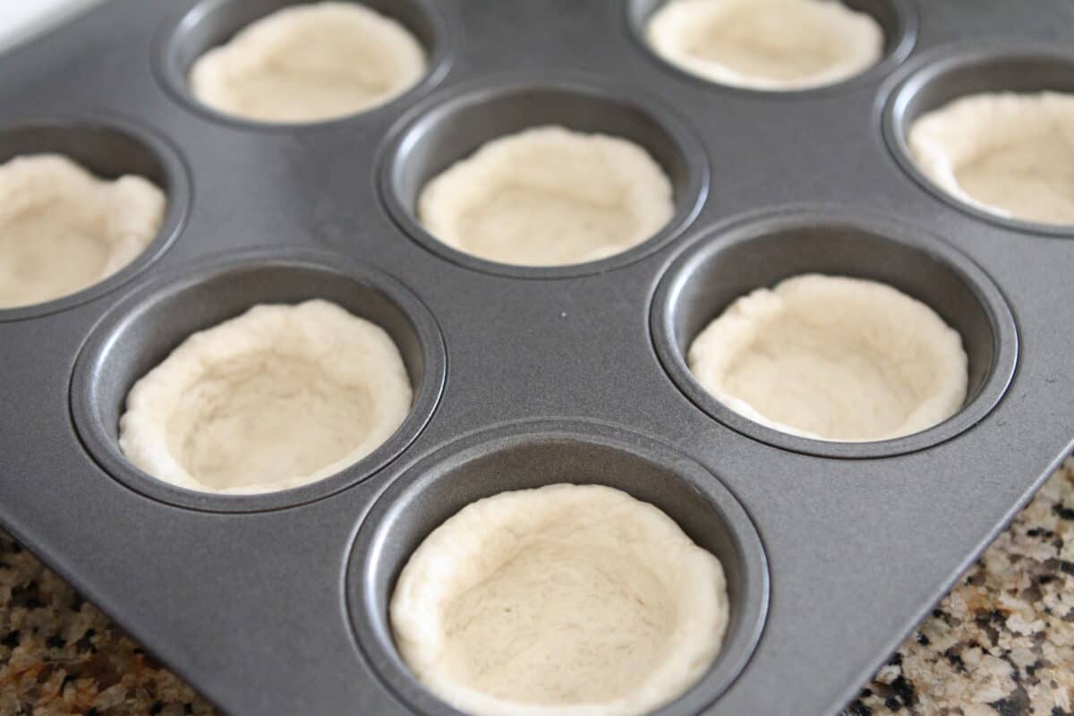 pressing bread dough into muffin tin