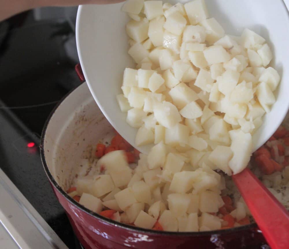 adding potatoes to pot of beef stew
