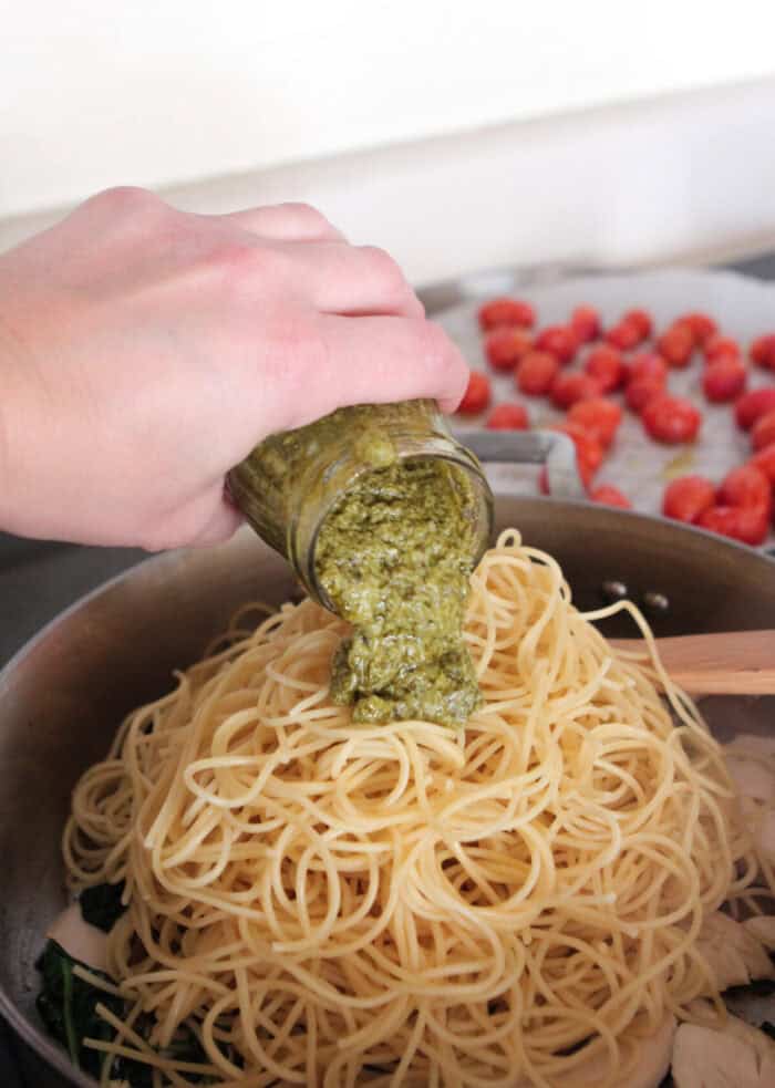 pouring pesto in pan of cooked spaghetti