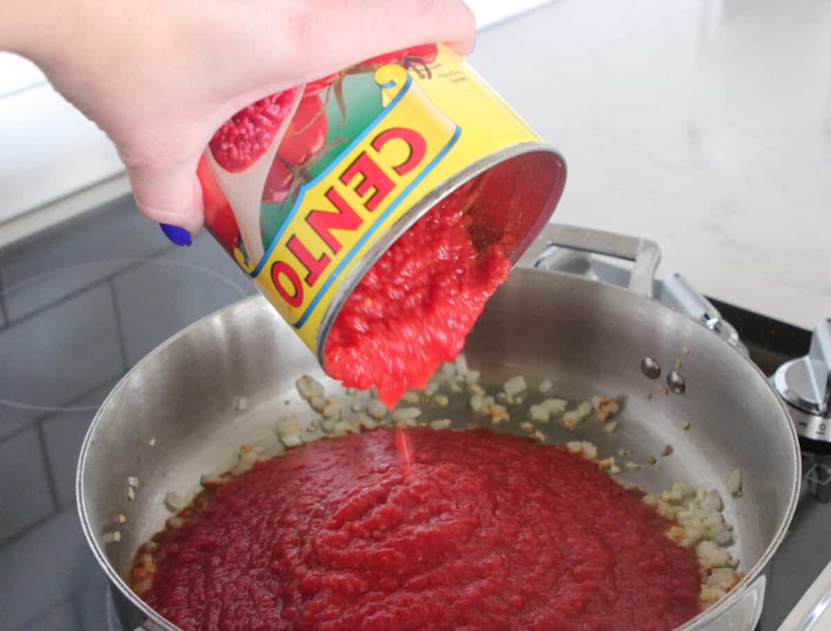 pouring crushed tomatoes in pan to make sauce
