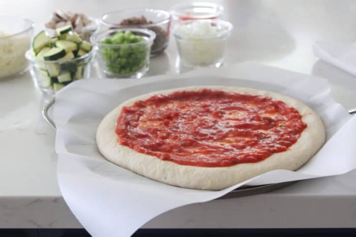 pizza sauce spread on pizza dough on pizza pan