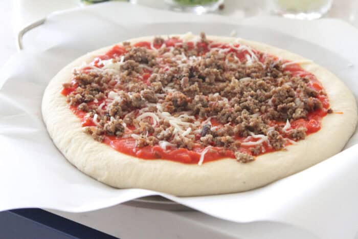 sausage added to supreme pizza on pizza pan
