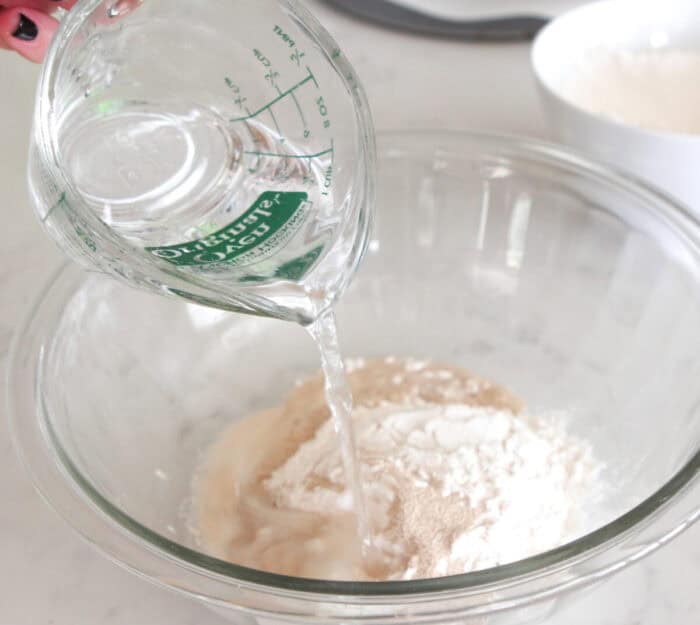 pouring warm water in mixing bowl for pizza crust