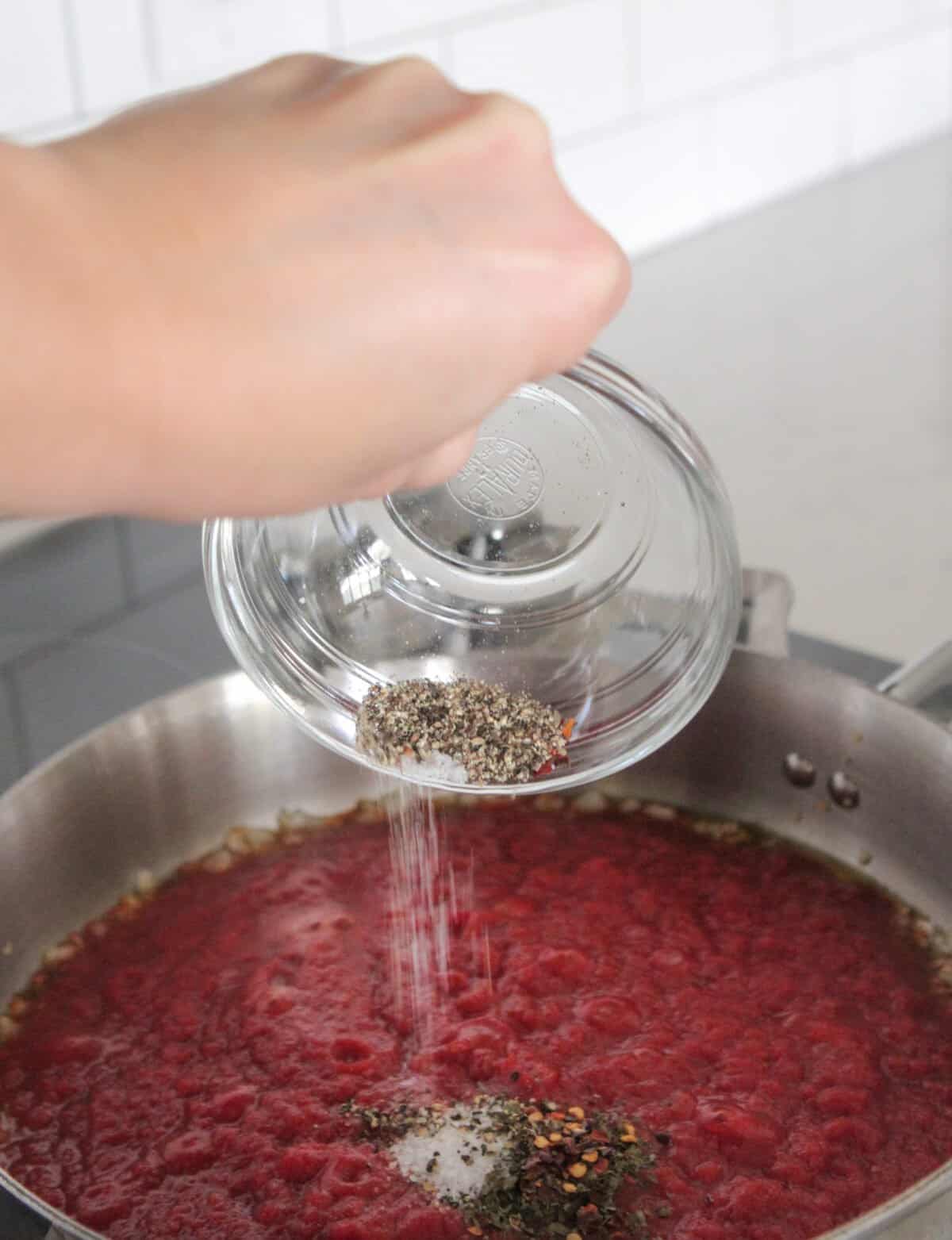 pouring seasoning into rigatoni pasta sauce