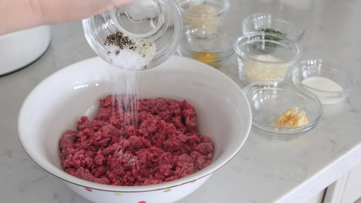 adding seasoning to ground beef in mixing bowl
