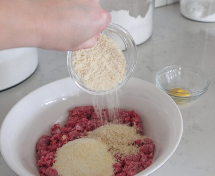 adding bread crumbs to meatball mixture in mixing bowl