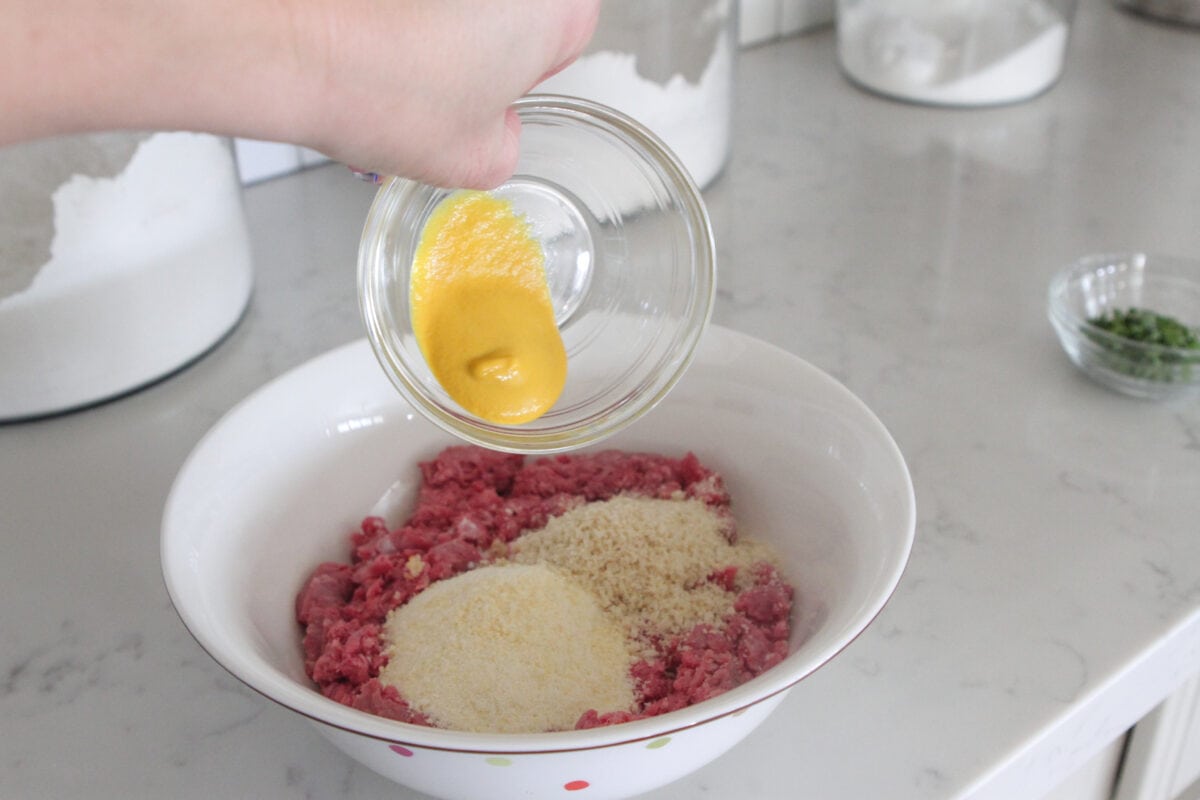 adding mustard to bowl of meatball mixture in mixing bowl