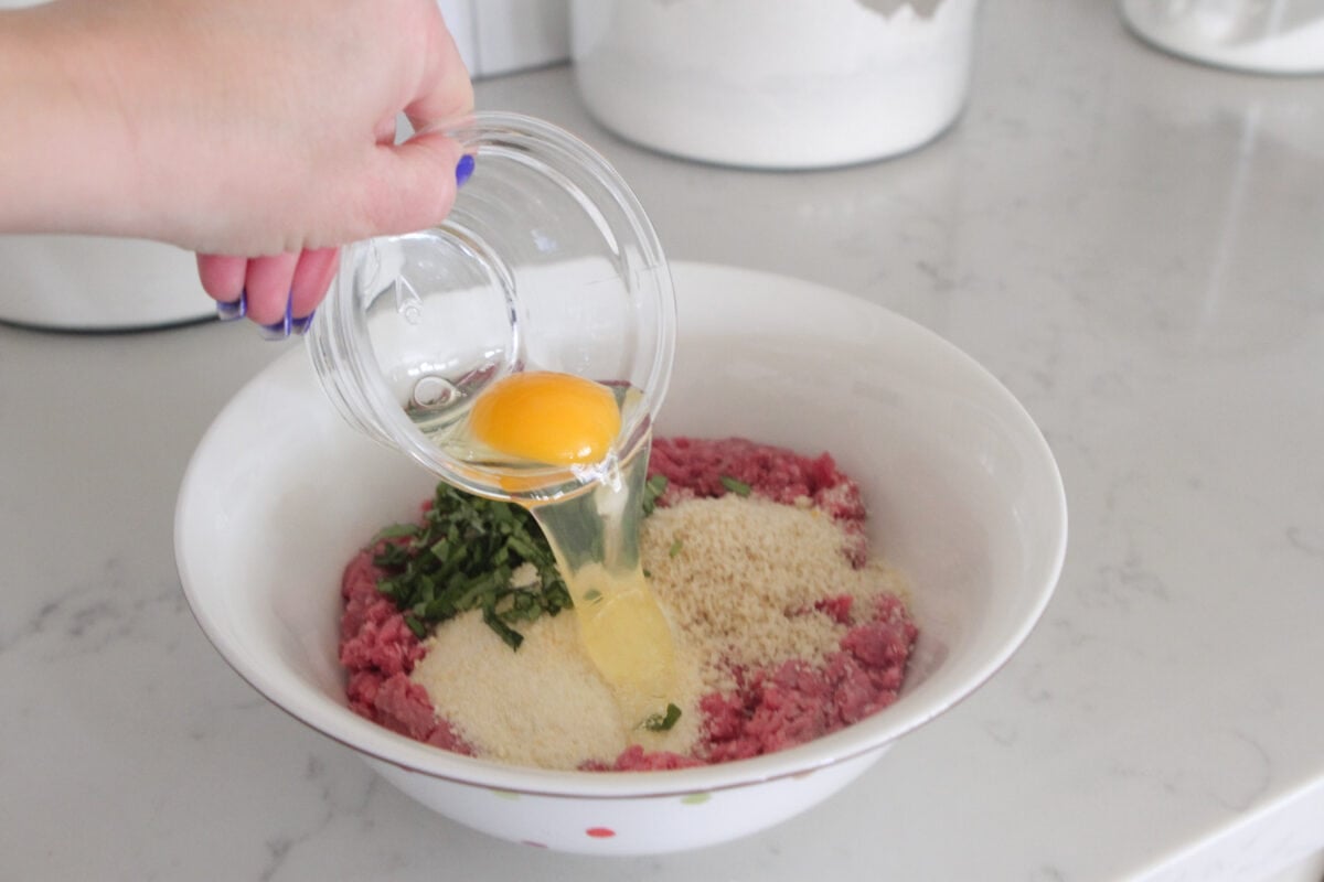 adding egg to bowl of meatball mixture