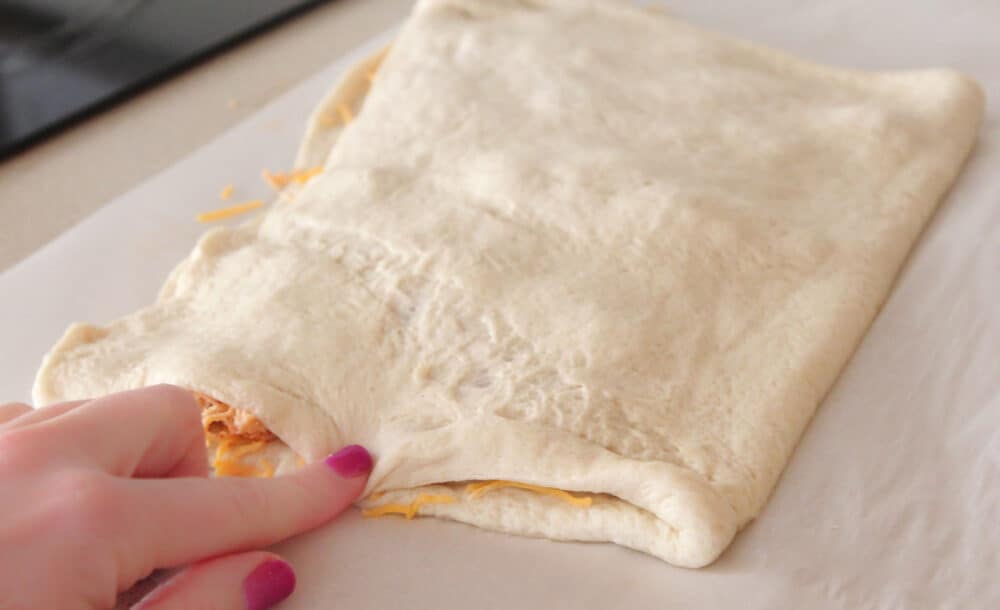 pressing pizza dough over chicken filling