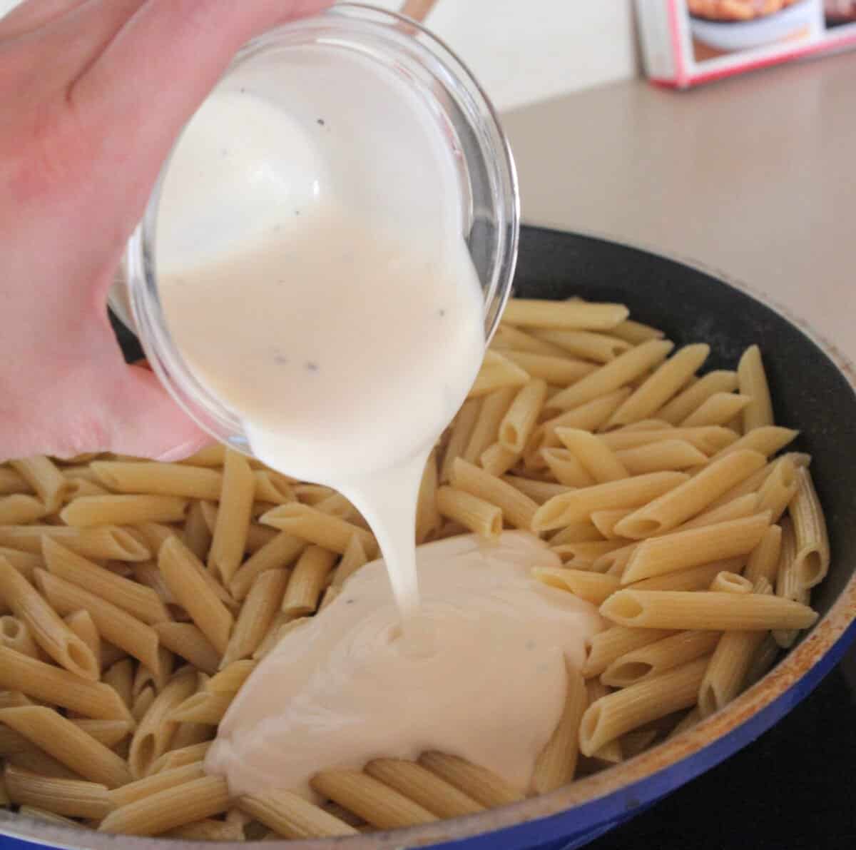 pouring alfredo sauce over pasta