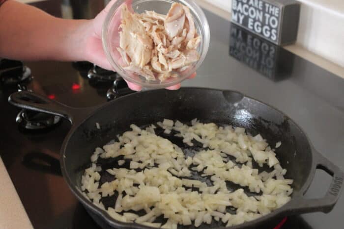 adding chicken to cooked onions in cast iron skillet