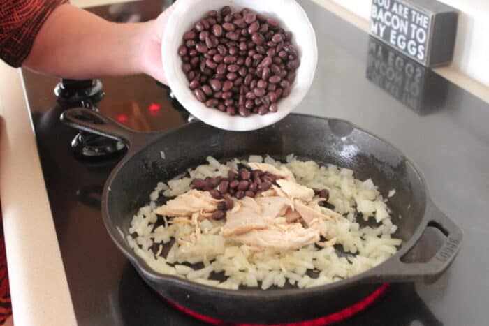 adding black beans to chicken taco bake mixture in cast iron skillet