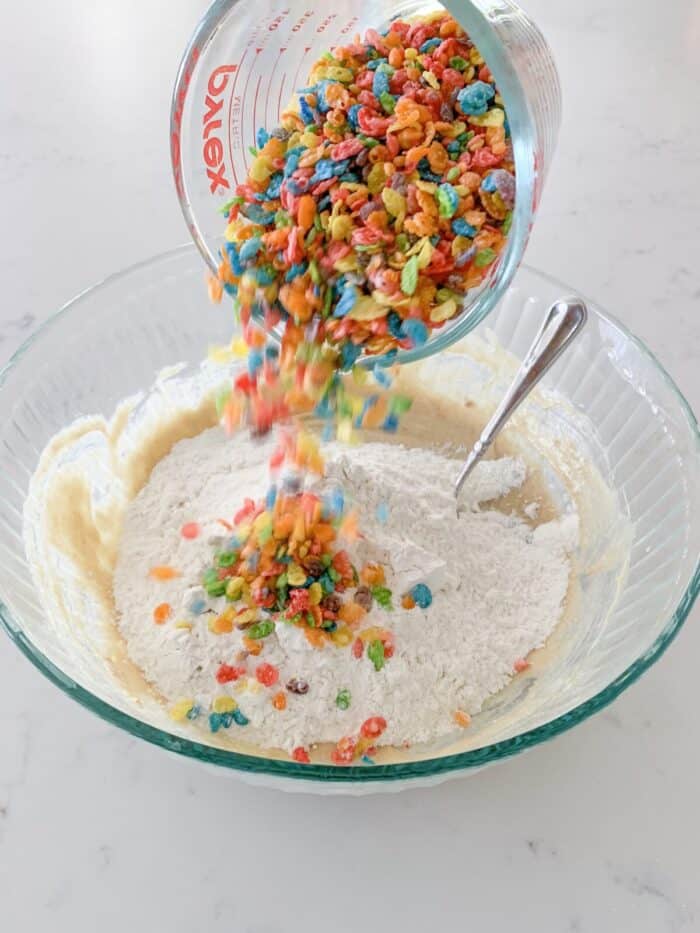 adding fruity pebbles to mixing bowl of cookie dough