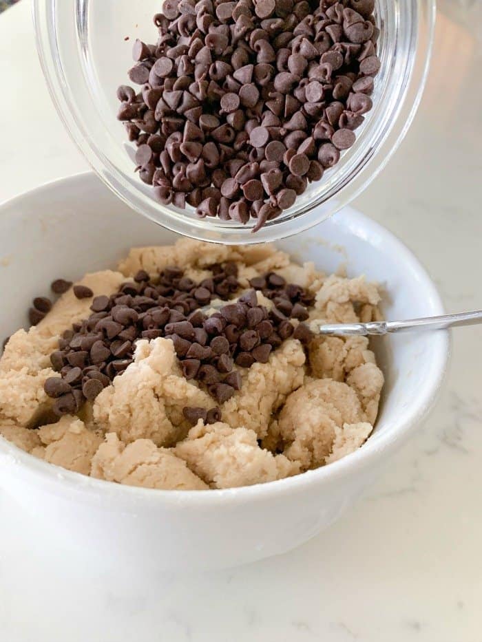Chocolate chips being added to a bowl of edible cookie dough