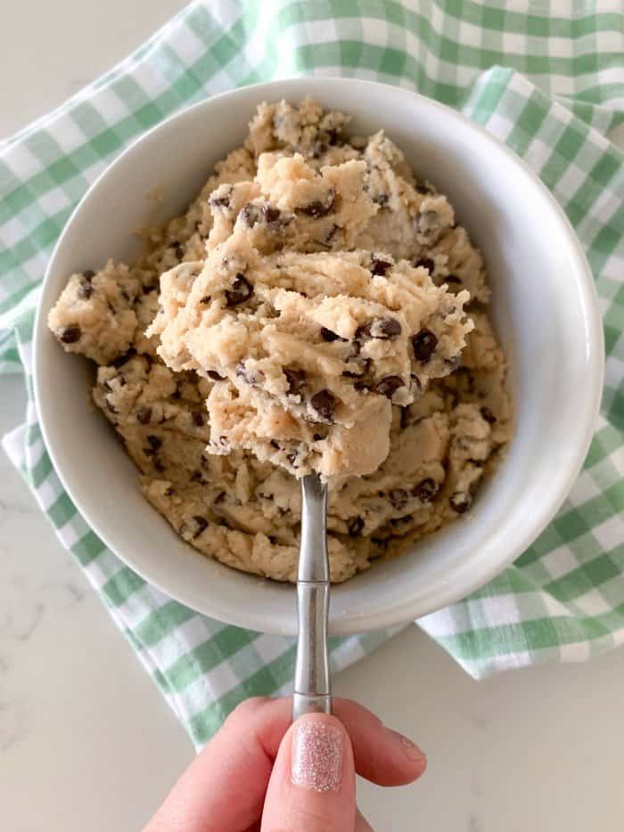 A spoon taking a scoop of edible cookie dough out of a bowl